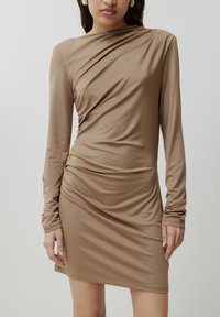 Langärmliges Kleid in Hellbraun, aus dehnbarem Material gefertigt. Verfügt über eine geraffte Detail am Taillenbereich und eine taillierte Silhouette. Glatte Textur.