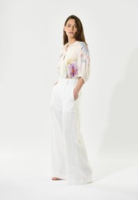 Bluse med blomsterprint, let og med korte pufærmer, parret med løse, højtaljede hvide linnedbukser med sidelommer.