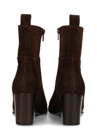 Botas de tobillo de ante marrón con un tacón de madera apilado, cremalleras laterales y una pestaña en la parte posterior. Textura suave y diseño elegante.