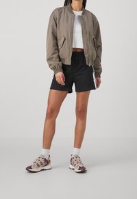 Bomber jacket in olive green, white cropped top, black shorts, and multicolored sneakers. Jacket has ribbed cuffs and side pockets.