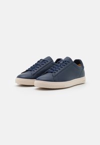 Zapatillas de piel azul marino con punta redonda, suela de goma beige plana y cordones a juego. Diseño minimalista con ligeros acentos de costura.