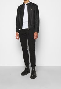 Czarna kurtka typu bomber z zamkiem błyskawicznym i złotymi akcentami, zestawiona z czarnymi spodniami cargo i botkami za kostkę. Gładka tekstura, dopasowany krój.