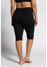 Leggings capri neri realizzati in tessuto elasticizzato, con vita elastica e una vestibilità aderente. Il modello è scalzo e di spalle.