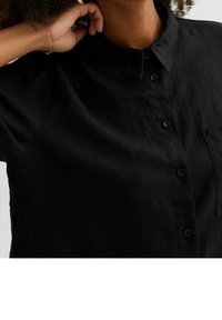 Chemise en lin noir à boutons avec col, manches courtes et poche poitrine, présentant une finition texturée et cinq boutons noirs.