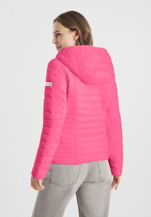 Vrouw draagt een felroze doorgestikte jas met capuchon en lichtgrijze spijkerbroek, gezien van achteren en kijkt zijwaarts.