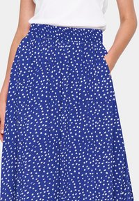 Modrá sukně s puntíky vyrobená z lehkého materiálu, s elastickým pasem a bočními kapsami. Klasický A-čkový střih se záhyby.
