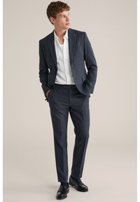 Tumši zils kostīms ar rūtiņu rakstu un piegrieztu formu, kopā ar baltu pogājamu kreklu un melnām loafer apaviem. Gluda auduma tekstūra ar strukturētu dizainu.