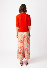 Red textured knit sweater with short sleeves paired with wide floral-patterned trousers in pastel shades, featuring pink and orange accents.