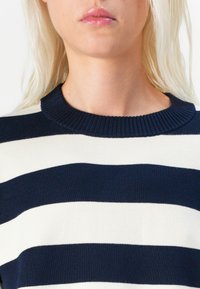 Pulover tricotat în dungi bleumarin și crem cu guler în nervuri. Prezintă dungi orizontale și un material moale, texturat. Design cu guler înalt.