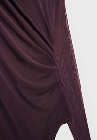 Viininpunainen pitkähiha paita, jossa on kerätyt sivut, valmistettu pehmeästä kankaasta. Siinä on resoripinta ja epäsymmetrinen helma.