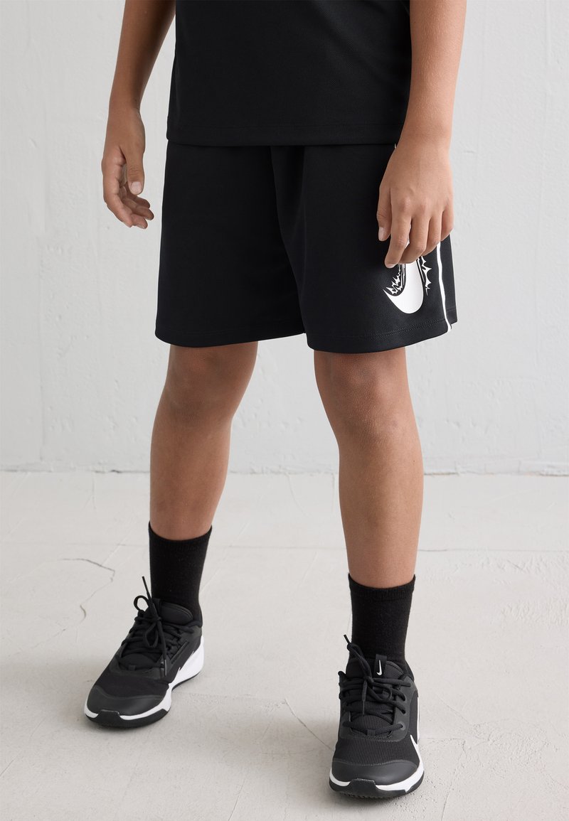 Pantalones cortos deportivos negros con un logo blanco, combinados con calcetines negros y zapatillas grises. Los pantalones cortos tienen un corte relajado y una textura suave.