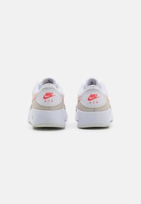 Nike tenisice s bijelim mrežastim gornjištem, ružičastim i sivim detaljima, podstavljenim ovratnikom i teksturiranom gumiranom potplatu. Logo prikazan na peti.