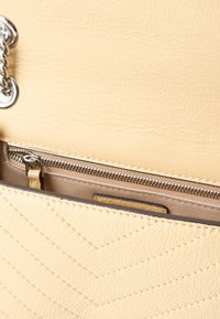 Bolsa de mão amarela em couro sintético com padrão de chevron acolchoado, ferragens prateadas e um bolso interior com fecho éclair.