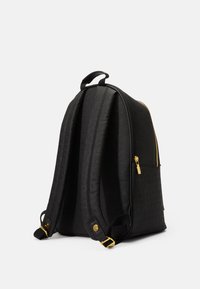 Svart ryggsekk med teksturert materiale, buet form, gullfarget glidelåsdetaljer, og justerbare polstrede skulderstropper. Inkluderer et håndtak på toppen for bæring.