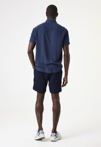 Chemise à manches courtes bleu marine avec un motif à rayures verticales subtiles, associée à un short texturé bleu marine et des baskets gris clair.