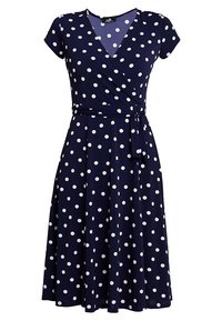 Granatowa sukienka w groszki z kopertowym fasonem, krótkimi rękawami i wiązaniem w talii. Wykonana z miękkiego materiału z lejącym się dołem.
