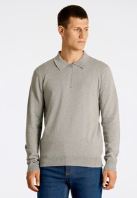 Ljusgrå långärmad polo-tröja med dragkedja i halsen, med ribbad fåll och ärmslut. Mjuk textur med en diskret logotypdetalj.