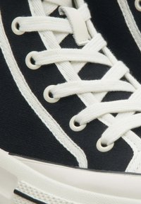 Czarne płótno sneakersy z białymi sznurówkami, oczkami i paskami po bokach; gumowa podeszwa; teksturowany materiał i kontrastowe przeszycia.