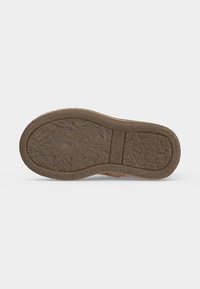 Semelle d'une chaussure marron avec une bande de roulement texturée et un petit logo circulaire près de la voûte plantaire sur un fond blanc uni.