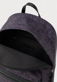 Plecak z otwartą główną komorą, ukazującą czarną wnętrze i kieszeń na zamek, ciemnofioletowy materiał z abstrakcyjnym wzorem oraz czarną rączką do noszenia.