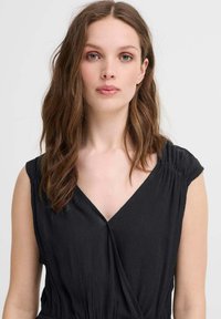 Rochie neagră cu decolteu în V și mâneci scurte, având un material texturat. Designul are detalii pliate la umeri.