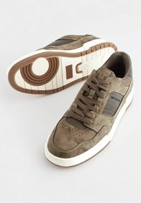 Oliwkowe zamszowe sneakersy z ciemnobrązowymi akcentami, perforowanym czubkiem, sznurowanym designem i teksturowaną gumową podeszwą.
