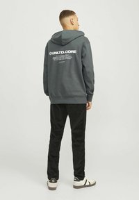 Grijze hoodie met een grote witte print op de achterkant, gecombineerd met zwarte corduroy broek en witte sneakers met zwarte accenten.