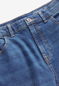 Straight Fit Denim-Jeans in mittlerem Blau mit orangefarbenen Nähten, Knopfverschluss und Fünf-Taschen-Design, mit einer glatten, leicht strukturierten Oberfläche.