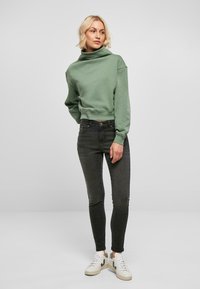 Sudadera corta de color verde claro con cuello alto tipo cowl. Combinada con jeans ajustados grises oscuros y zapatillas blancas con toques verdes.