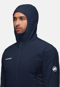 Navy blue hooded jacket with zip closure, soft material, and fitted design. Features Mammut logo on the chest and shoulder.
