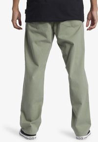 Pantaloni din bumbac de culoare verde deschis, cu croială lejeră și picior drept. Prezintă buzunare la spate și o textură subtilă; asortați cu adidași negri cu talpă joasă.