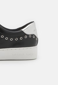 Baskets en cuir noir avec des accents argentés, des œillets pour les lacets, une semelle texturée blanche et "MICHAEL KORS" embossé au talon.