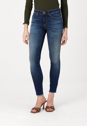 Smaljeans i mørkeblå denim med en slitt vask, med høy midje og flisede sømmer. Kombinert med brune hælsandaler.