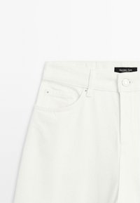 Pantaloni in denim bianco con un classico design a cinque tasche, cuciture definite, chiusura con bottone e un'etichetta nera sulla vita.
