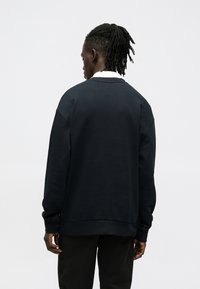 Sudadera azul marino con hombros caídos y puños acanalados, que presenta un cuello alto y una textura suave, combinada con pantalones negros.