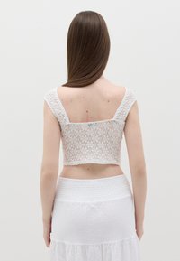 Top corto bianco in pizzo con motivo floreale testurizzato, spalline larghe e orlo dritto. Abbinato a una gonna bianca con vita elasticizzata testurizzata.