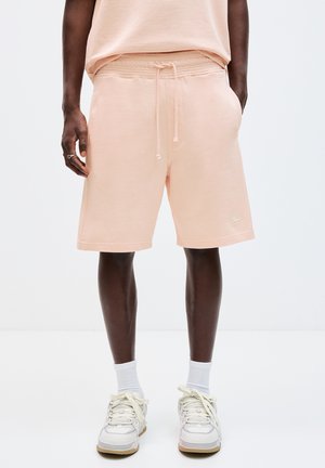Persikofärgade bomullsblandade shorts med elastisk midja, dragsko, sidofickor och en liten logotypdetalj. Matchas med vita sneakers och strumpor.