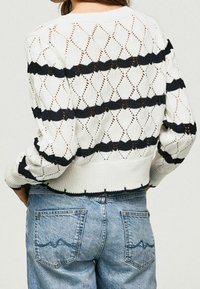 Suéter blanco de punto con patrones en forma de diamante y rayas marinas, con un dobladillo acanalado y mangas largas; llevado con jeans de tiro alto en azul claro.