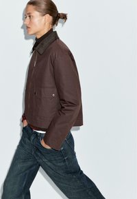 Braune cropped Jacke mit einem Cordkragen, Fronttaschen und einem Reißverschluss, kombiniert mit lockeren blauen Jeans.