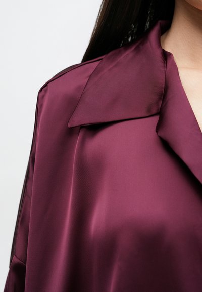 Bordo spalvos sateninė striukė, turinti platų apykaklę ir lygią tekstūrą, matomomis siūlėmis ir laisvo kirpimo.