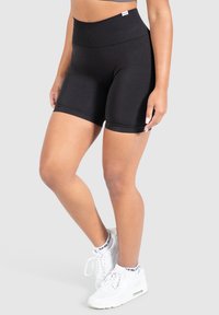 Černé stahovací kraťasy s vysokým pasem, hladkým povrchem a minimem švů, doplněné bílými sportovními teniskami.