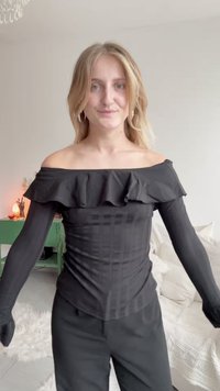 Svart av-shoulder topp med volangkant, lange tettsittende ermer og teksturert stoff med vertikale striper.