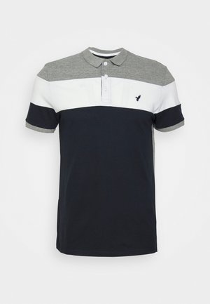Polo avec col et épaules gris, bande blanche sur la poitrine, corps et manches bleu marine, avec un petit logo oiseau sombre sur la poitrine gauche.