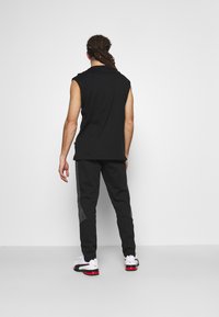 Top senza maniche nero con vestibilità rilassata, abbinato a pantaloni jogger neri con dettagli grigi sui lati e scarpe sportive bianche.