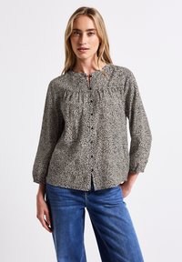 Beige blus med svart djurmönster, med knäppning fram, rynkad halslinning och långa ärmar, kombinerad med blå denimjeans.