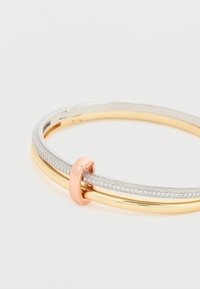 Bracelet double jonc en or et argent avec un accent en boucle en or rose sur fond blanc.