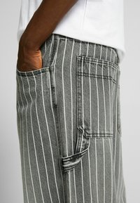 Pantaloni cargo a righe grigio scuro realizzati in denim, con strisce verticali bianche, tasche laterali e una finitura texturizzata.