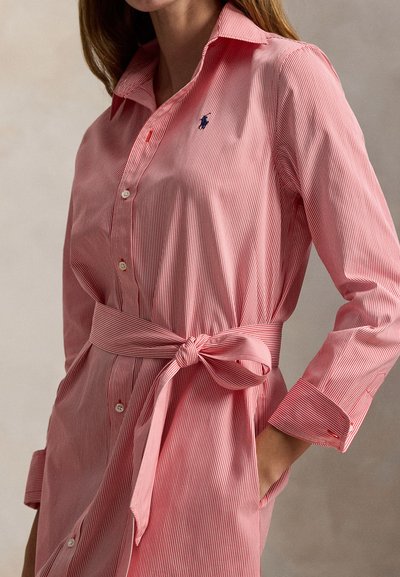 Φόρεμα πουκάμισο με κόκκινες και λευκές ρίγες, λαιμόκοψη με γιακά, κουμπιά μπροστά και δεμένο στη μέση. Λείο ύφασμα με διακριτική λάμψη.