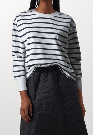 Chemise à manches longues bleu clair avec des rayures horizontales navy, col rond et poignets côtelés, associée à une jupe noire matelassée.