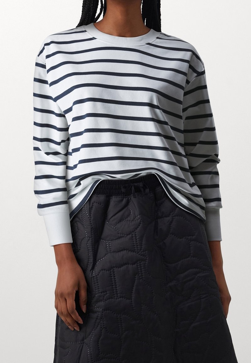 Camicia azzurro chiaro a maniche lunghe con strisce orizzontali blu navy, scollatura rotonda e polsini a costine, abbinata a una gonna nera trapuntata.